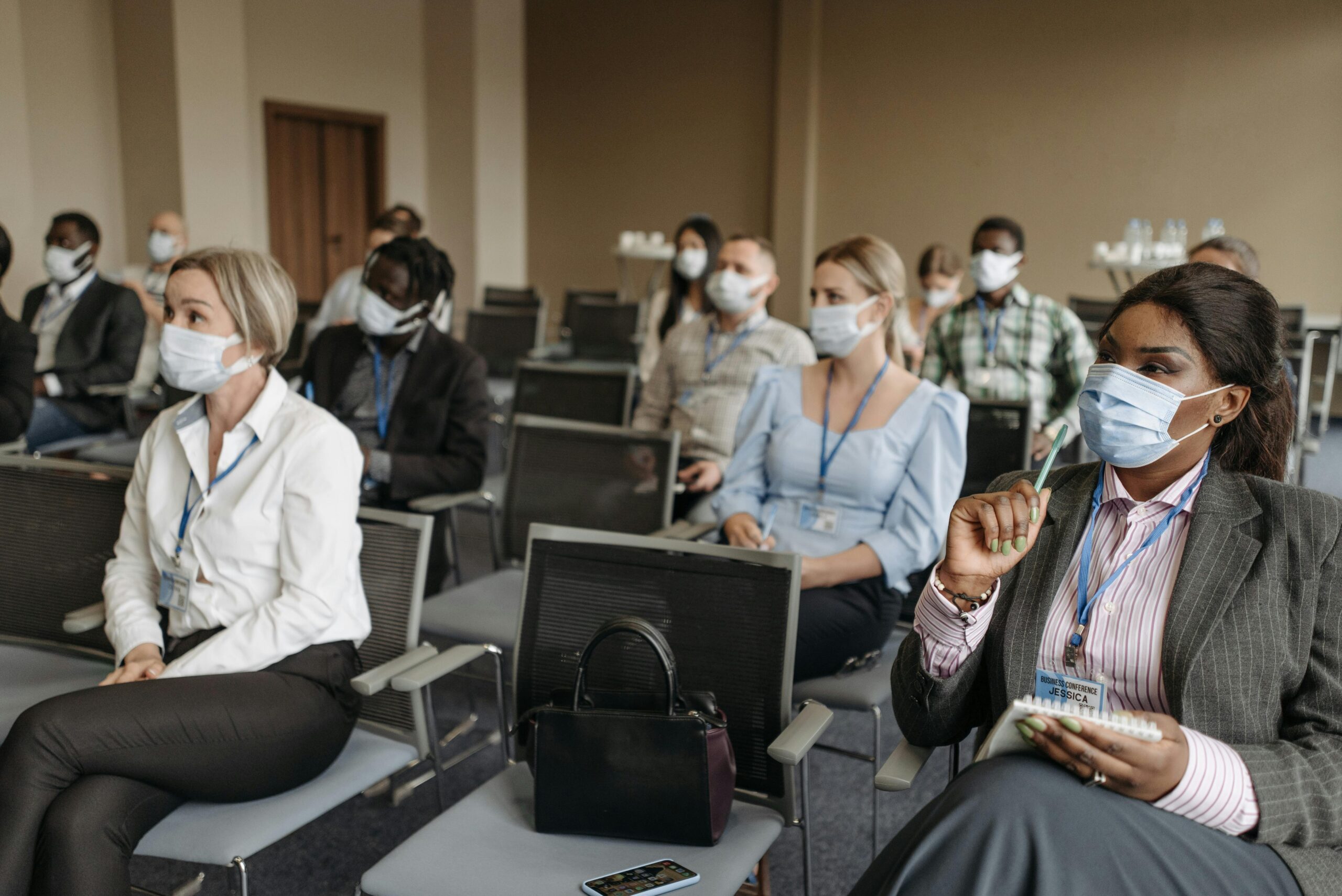 Diverse group of professionals in a conference room wearing face masks during a business seminar.